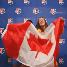 a woman is holding a canadian flag in front of a wall with logos for the women 's national league