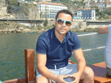 a man wearing sunglasses sits on a wooden railing overlooking a body of water