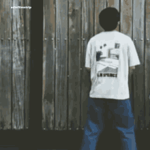 a man standing in front of a wooden fence wearing a white t-shirt that says la place on the back