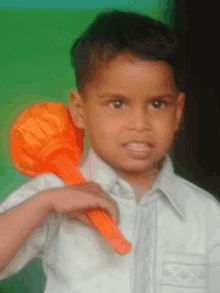 a young boy in a white shirt is holding an orange object on his shoulder