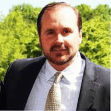 a man with a beard wearing a suit and tie is smiling .