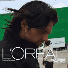 a man with long hair is standing in front of a l'oreal paris truck