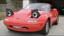 a red sports car with a funny face on it is parked in a driveway .