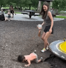 a woman is standing next to a child who is crawling on the ground in a playground .