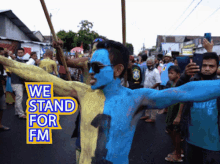 a man with blue paint on his face stands in front of a crowd with a sign that says we stand for fm