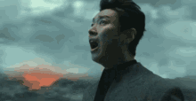 a man in a suit is standing in front of a volcano with his mouth wide open .