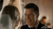 a man in a tuxedo and bow tie is smiling at a woman in a veil .