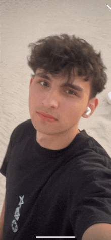 a young man taking a selfie on the beach wearing a black shirt