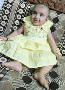 a baby in a yellow dress is sitting on a checkered couch