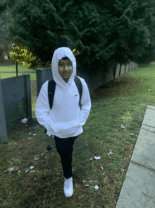 a boy wearing a white nike hoodie is walking down the sidewalk