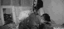 a black and white photo of a man and a woman having a pillow fight on a bed .