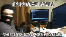 a man wearing a mask is sitting in front of two computer monitors with the words linux developers when trying to add features below him