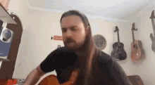 a man with long hair and a beard is playing a guitar in a room with guitars on the wall .