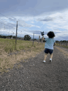 a little girl is running down a gravel road holding a toy