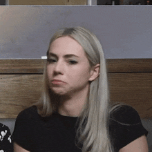 a woman with long blonde hair is making a funny face while sitting in front of a wooden table .