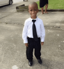 a young boy wearing a white shirt and black tie is standing on a sidewalk