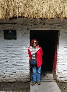 a woman stands in front of a thatched roofed building