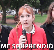 a woman in a red sweatshirt is holding a microphone and the words me sorprendio are above her