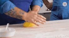 a man with a tattoo on his arm is kneading a yellow ball of dough on a wooden cutting board