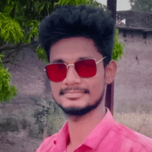 a man wearing red sunglasses and a pink shirt smiles for the camera