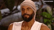 a man with a beard and a bandage on his head is wearing a white tank top .