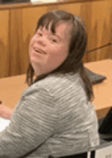 a woman with down syndrome is sitting in a wheelchair at a table and smiling .