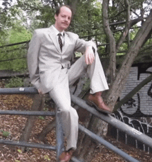 a man in a suit is sitting on a railing with his legs crossed