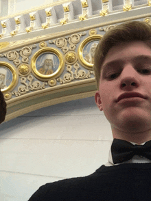 a young man in a bow tie stands in front of a ceiling with religious icons