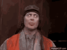 a man wearing an orange vest and a hat is making a face .