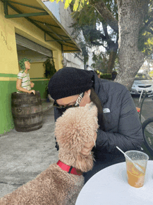 a woman wearing a black north face jacket kisses a small brown dog