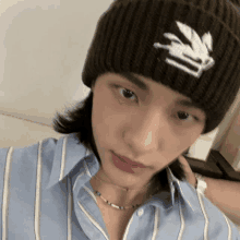 a young man wearing a striped shirt and a beanie is taking a selfie .