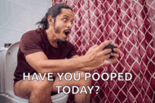 a man is sitting on a toilet playing a video game and asking if he has pooped today .