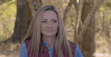 a woman in a red vest stands in front of trees with the cowboy way written on the bottom right