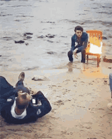 a man is laying on the beach taking a picture of a man sitting in a chair on a beach .