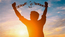 a silhouette of a man holding chains in his hands at sunset .