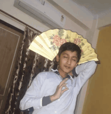 a young boy holds a fan over his head in front of an air conditioner