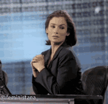 a woman in a suit is sitting at a desk with her hands folded in front of her face .