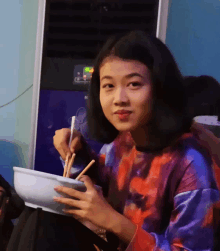 a woman eating a bowl of food with chopsticks in front of an air conditioner that says n on it