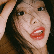 a close up of a woman 's face with her hair blowing in the wind and red lips .