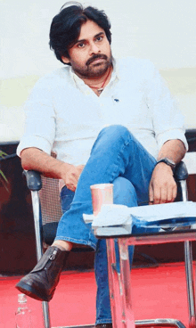 a man with a beard is sitting in a chair next to a table with a cup of coffee .