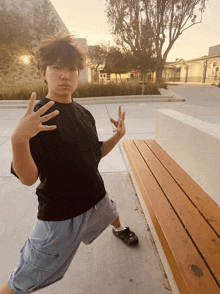 a young man in a black shirt and blue shorts is standing in front of a wooden bench