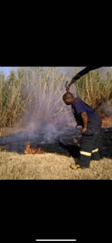 a man in overalls is standing in front of a fire in a field .