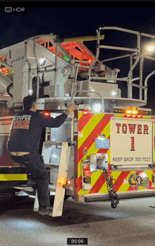 a man climbs up the ladder of a fire truck that says tower 1 on it