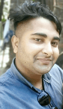 a man in a blue shirt and sunglasses smiles for the camera