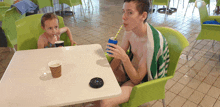 a boy and a girl sit at a table drinking through a straw