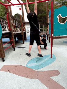 a man hangs upside down on a monkey bars while a child squats in the background