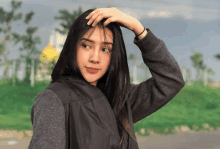 a young woman is touching her hair while standing in front of a green field .