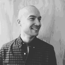 a bald man wearing a plaid shirt is smiling in a black and white photo .