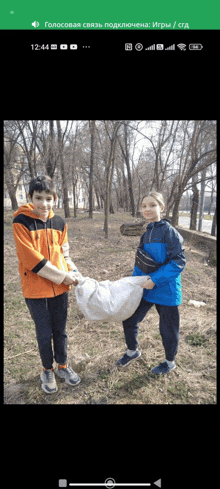 a boy in an orange jacket is holding a white bag next to a boy in a blue jacket