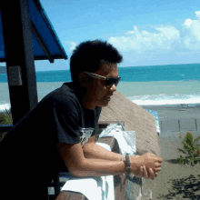 a man wearing sunglasses leans against a wooden railing overlooking the ocean